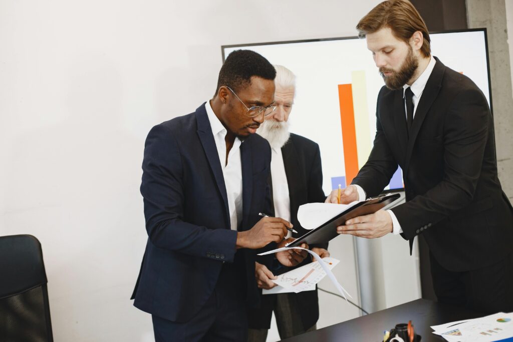 Three businessmen engaged in document signing in a modern office setting.